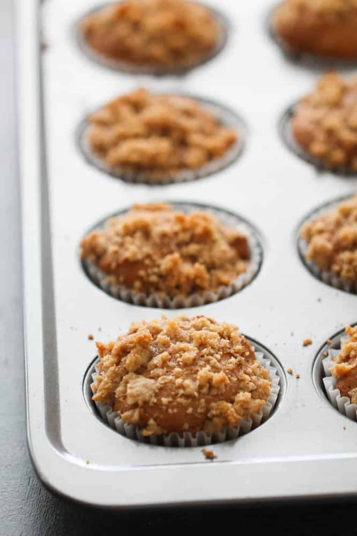 A muffin tray with eight freshly baked muffins topped with a crumbly streusel in paper liners.