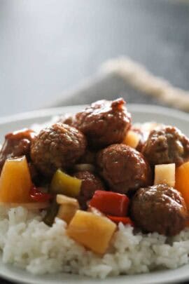 Plate of white rice topped with meatballs, bell peppers, and pineapple chunks, served in a sauce.