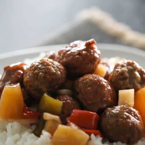 Plate of white rice topped with meatballs, bell peppers, and pineapple chunks, served in a sauce.