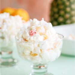 A glass filled with a serving of Easy Ambrosia Salad. With other glasses with servings in the background.