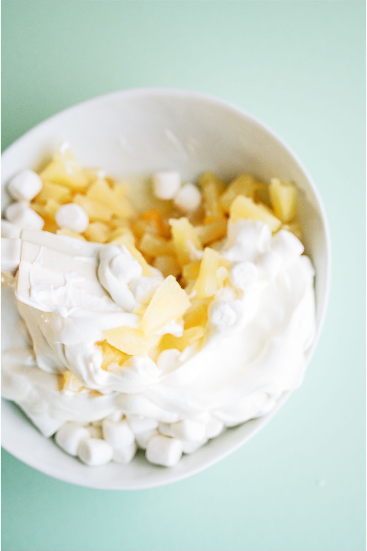 Vanilla yogurt added to fruit and marshmallows in mixing bowl.