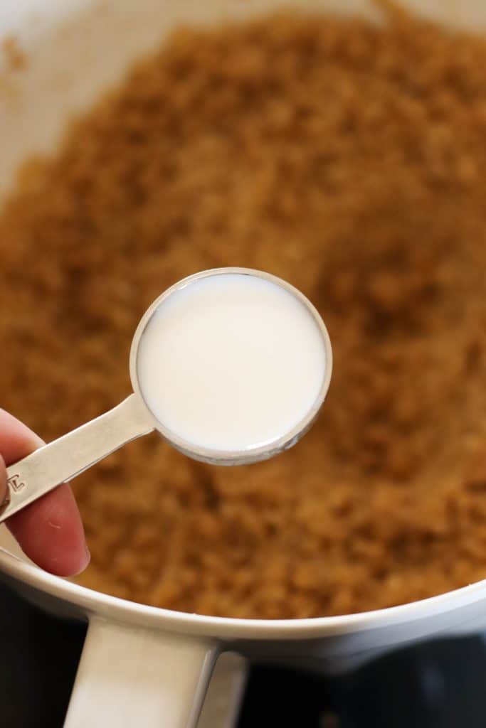 Milk in measuring tablespoon held aove the bowl of edible cookie dough.