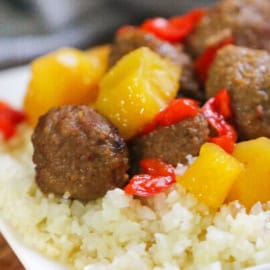 A close-up of a dish featuring meatballs, yellow pineapple chunks, and red bell peppers on a bed of rice.