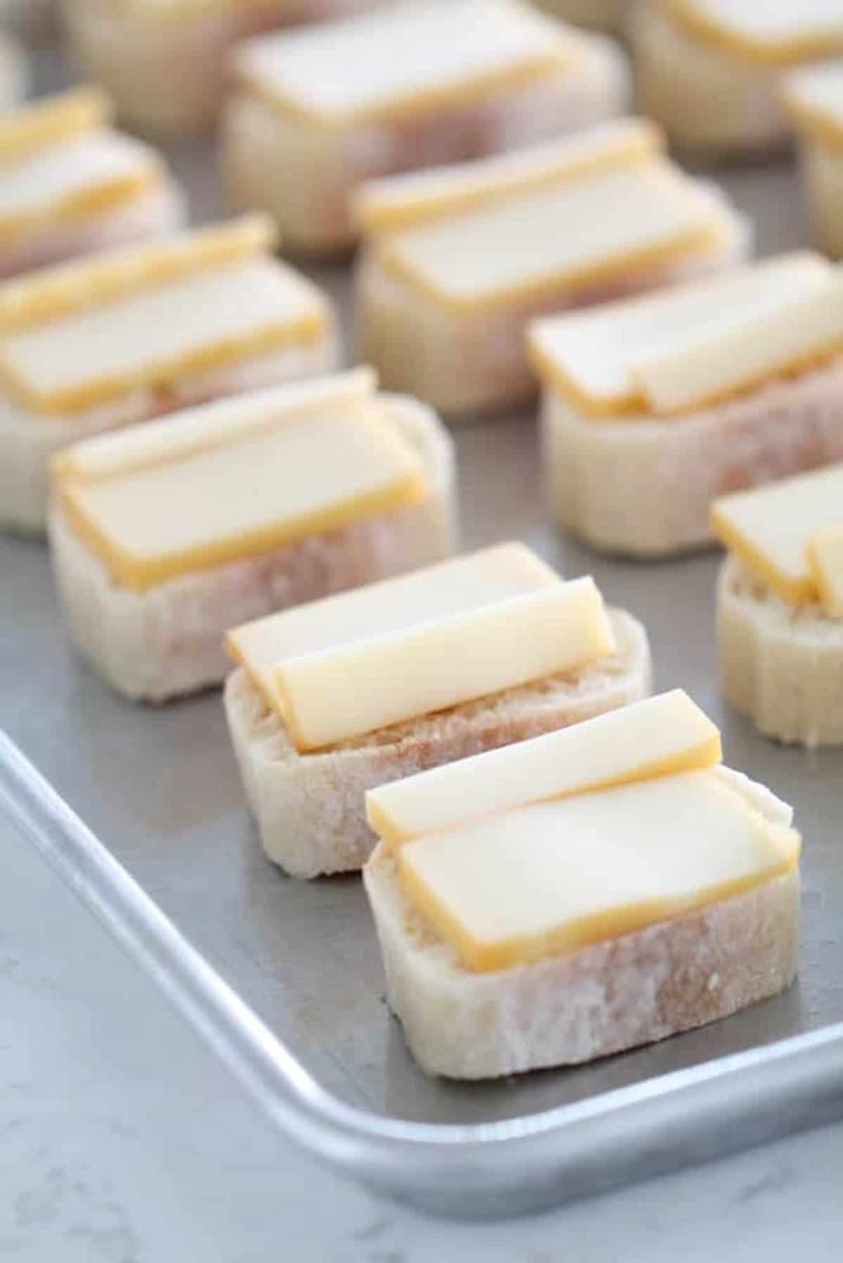 Slices of bread topped with cheese are neatly arranged on a baking sheet.