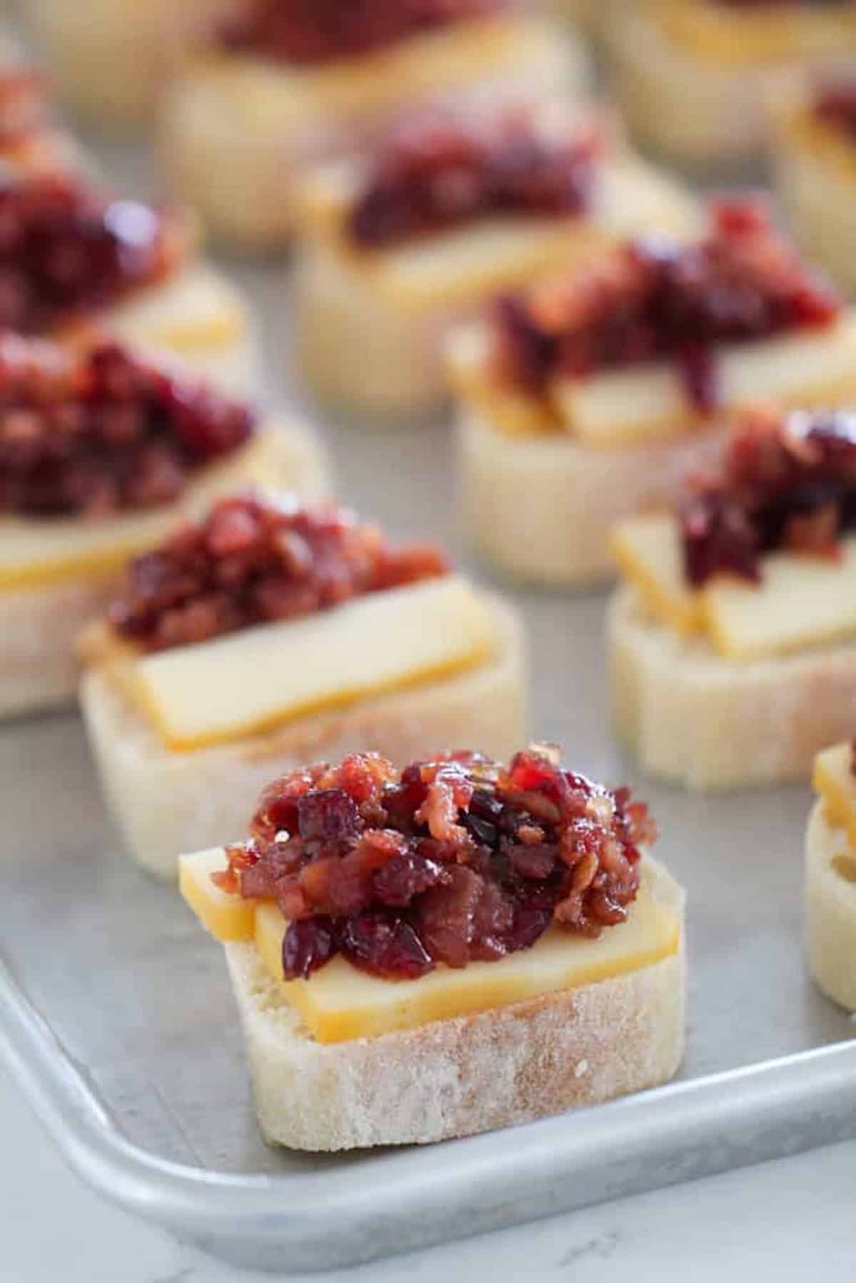 Slices of bread topped with cheese and a chutney or relish on a baking sheet.