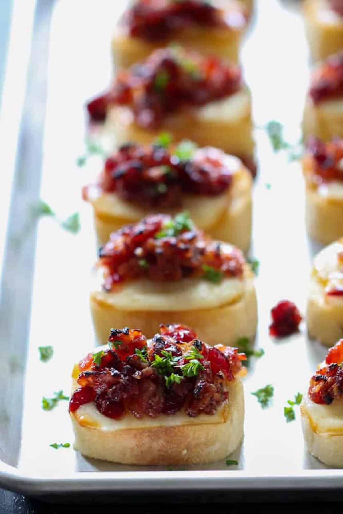 Toasted baguette slices topped with chopped tomatoes, herbs, and cheese, arranged in rows on a baking tray.