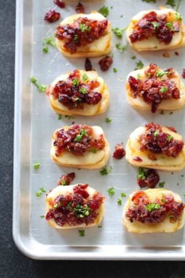 Tray of baked cranberry bacon jam crostinis topped with cheese, bacon, and parsley.