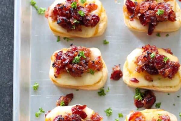 Tray of baked cranberry bacon jam crostinis topped with cheese, bacon, and parsley.