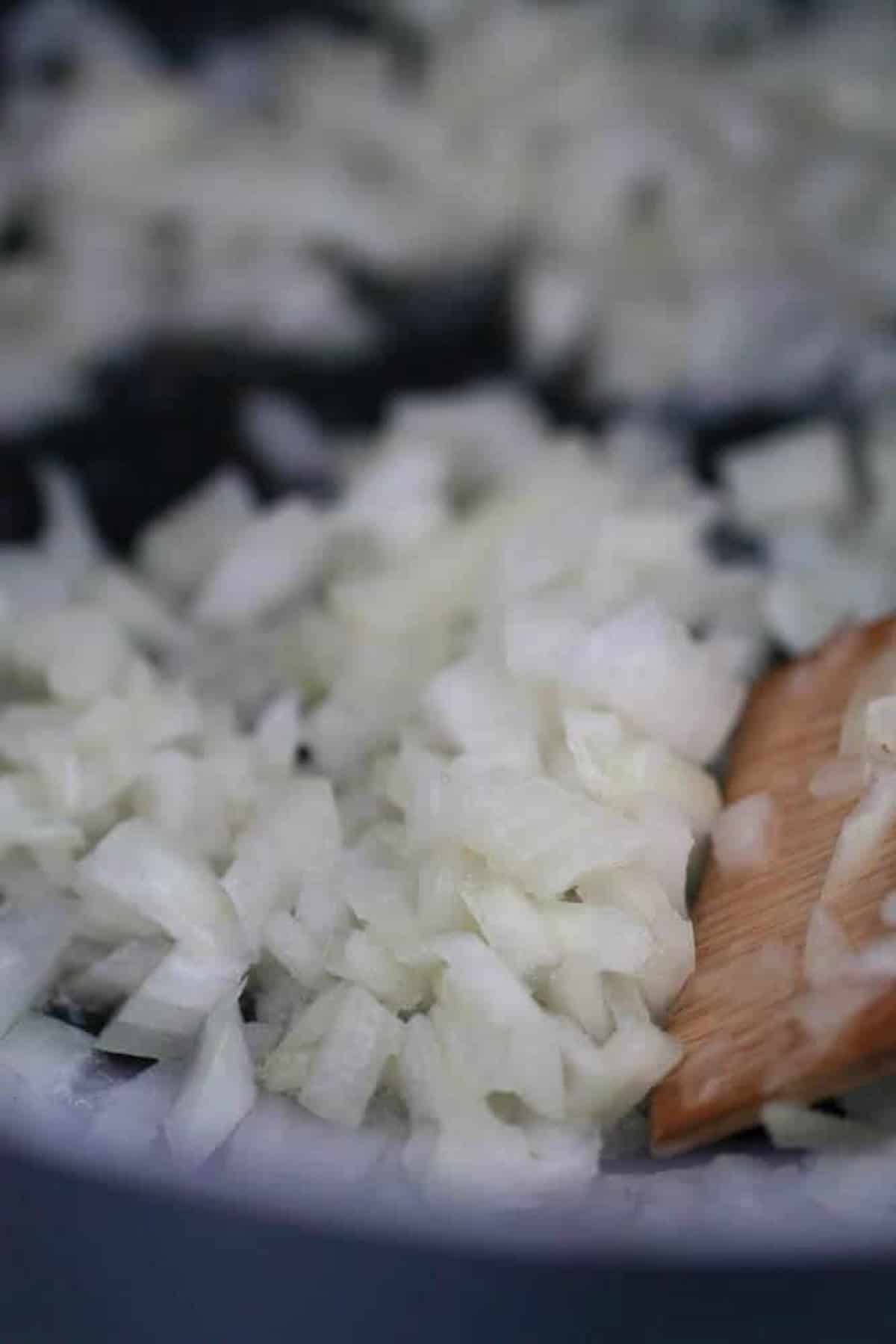 Diced onions being sautéed in a pan with a wooden spatula.