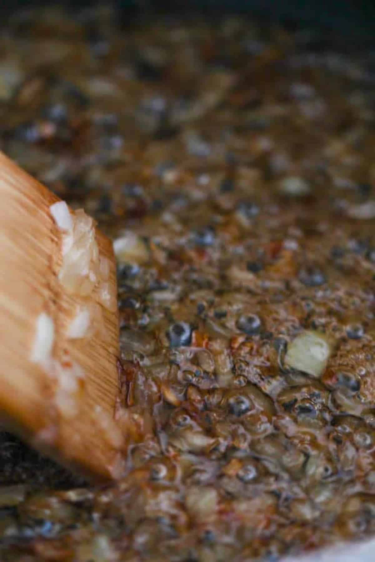 A wooden spatula stirs chopped onions cooking in a pan with bubbling oil.