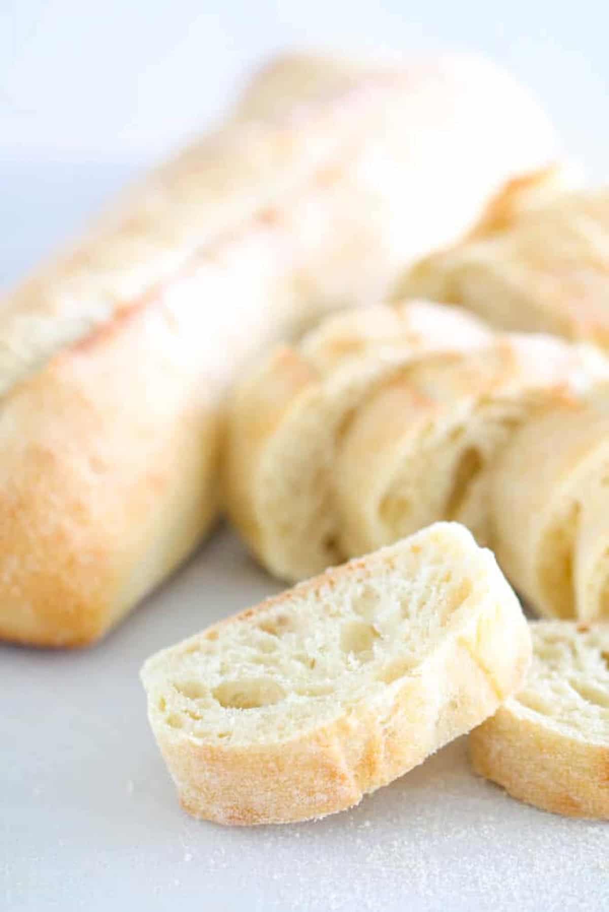 Sliced baguette pieces on a white surface, with an unsliced baguette in the background.