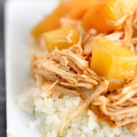 Shredded chicken and pineapple chunks served over a bed of white rice on a white plate.