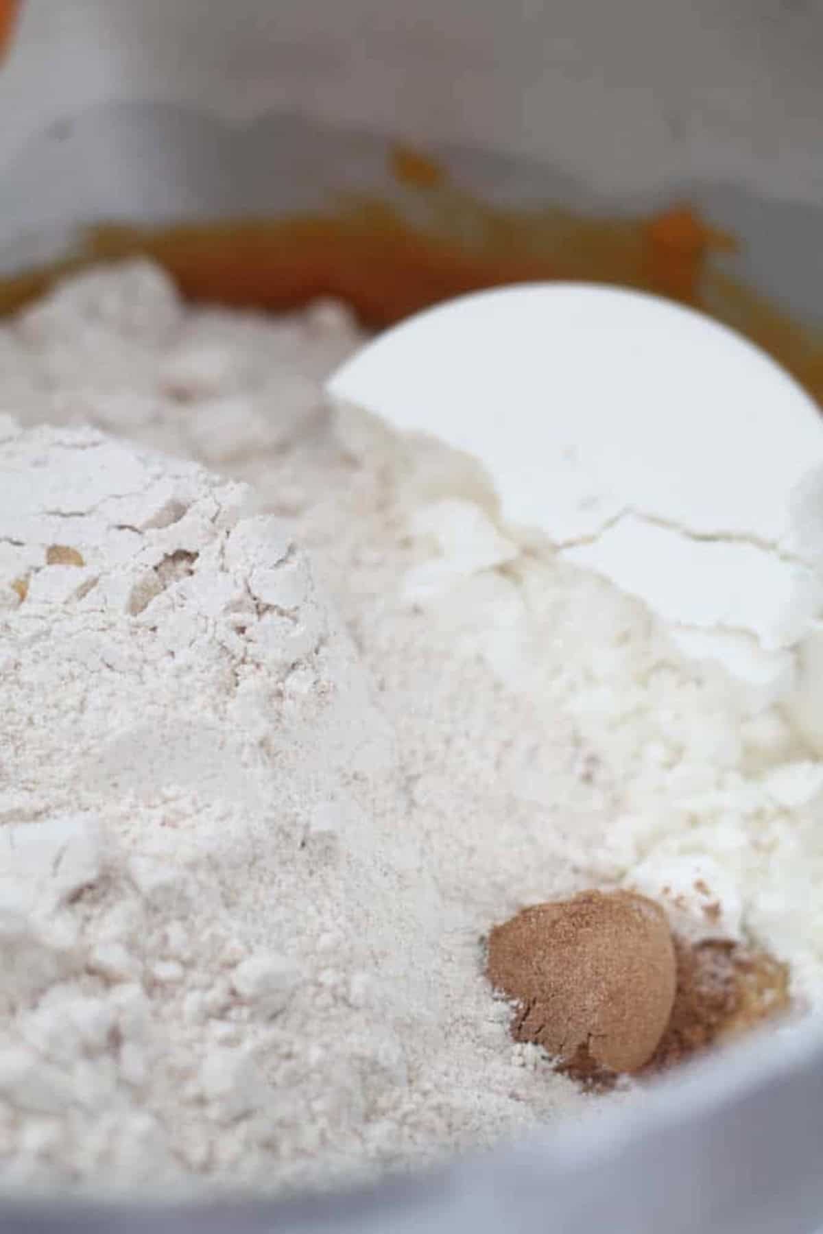 A close-up of a bowl containing flour, sugar, and a scoop of spice, likely for baking.