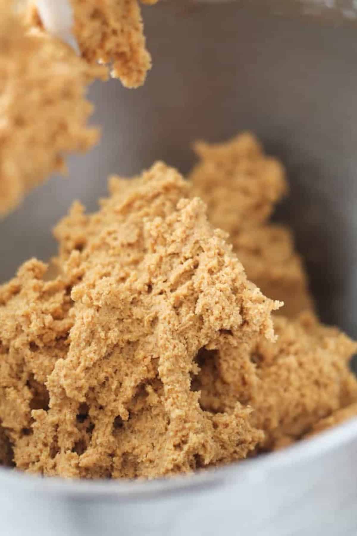 Close-up of light brown cookie dough being mixed in a bowl, showing the texture and consistency of the dough.