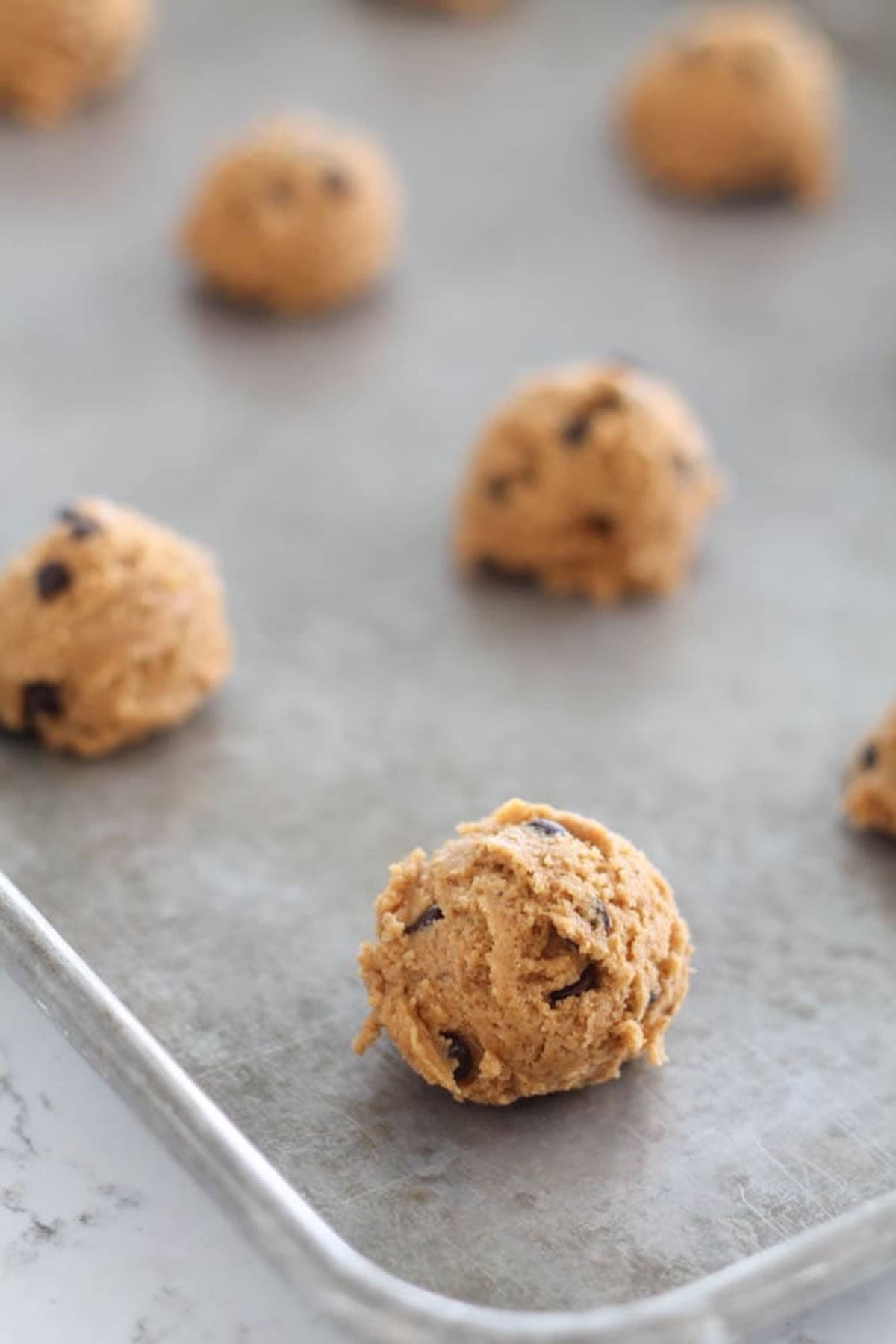 Close-up of raw chocolate chip cookie dough balls arranged on a baking sheet, ready to be baked.