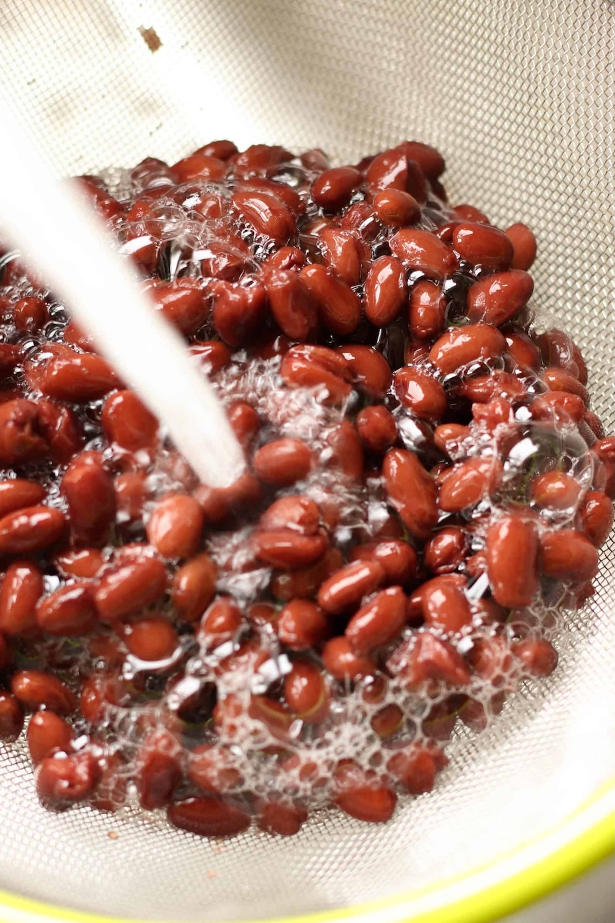 Red beans being rinsed under running water in a mesh strainer.