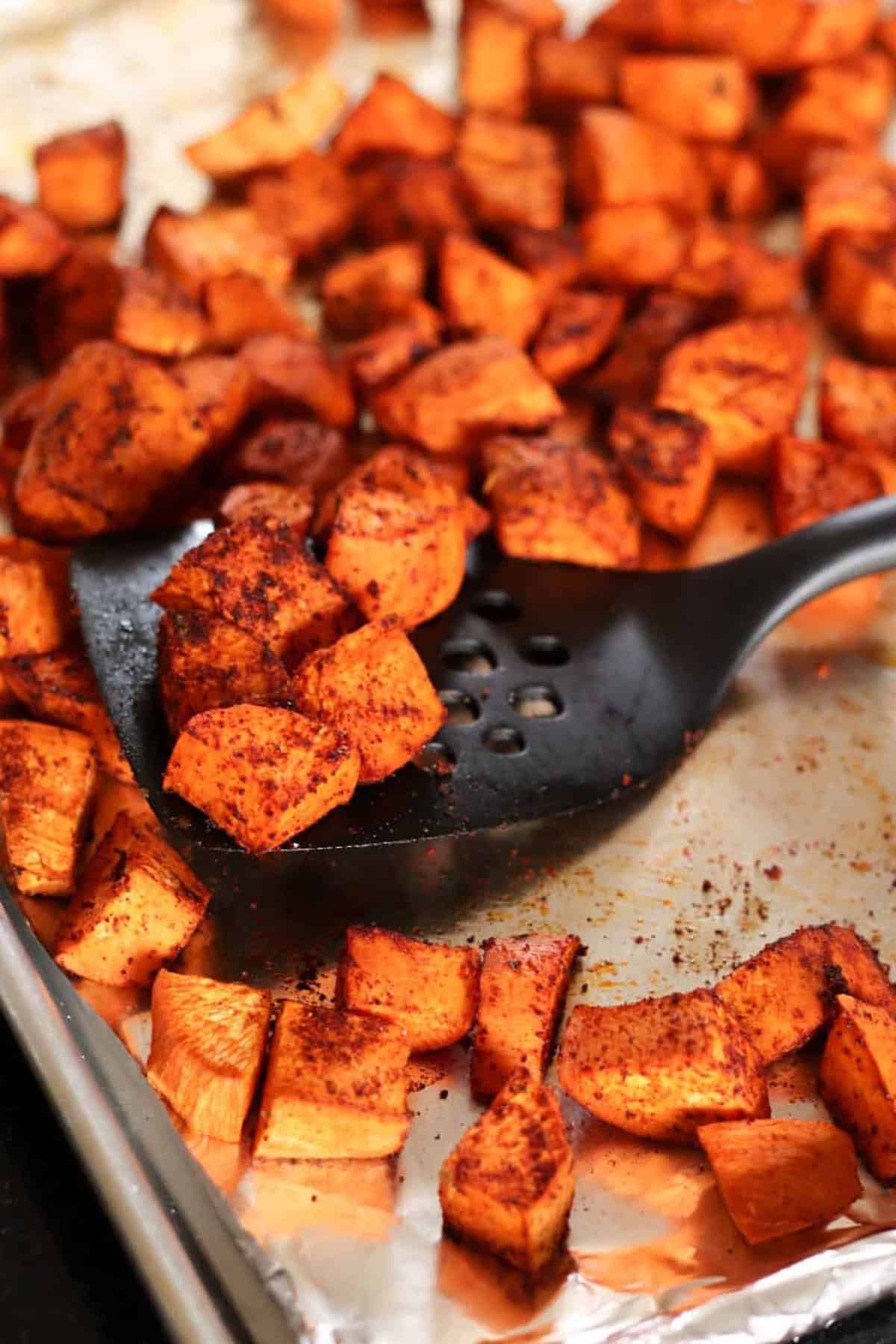 Diced sweet potatoes seasoned and roasted on a baking sheet with a black spatula.