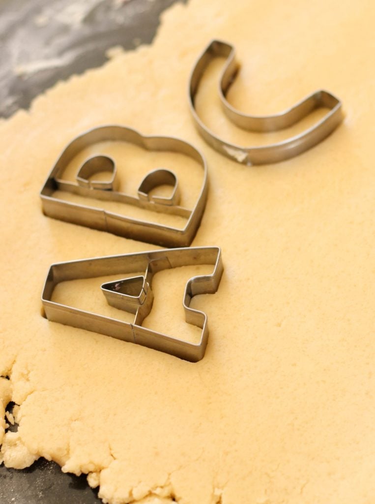 Sugar Cookie dough rolled out with alphabet letter cookie cutters sitting on top.