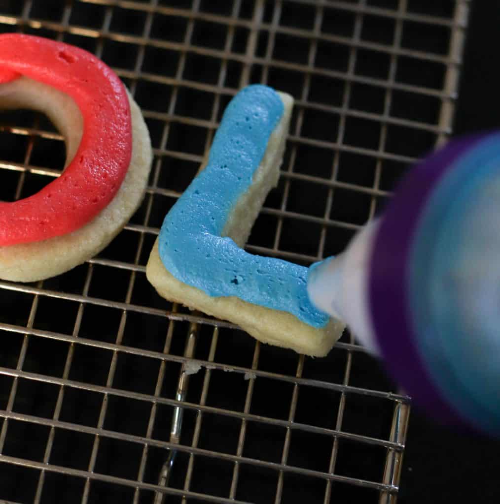 Using a bottle to apply colored buttercream frosting to alphabet shaped cookies.