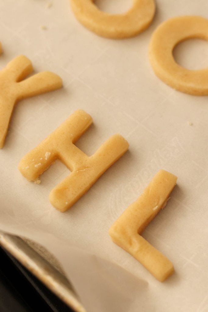 Letter shaped sugar cookie dough cut out and on a baking sheet lined with parchment paper.