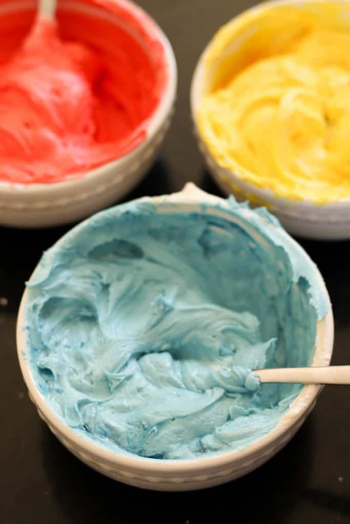 3 bowls of buttercream frosting in different colors.