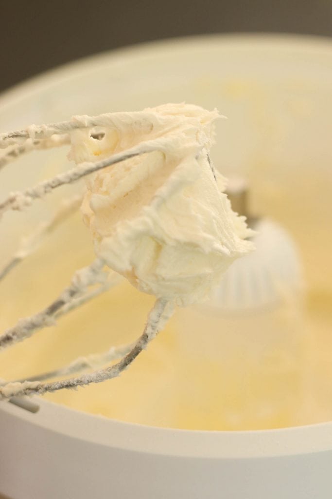 Buttercream frosting mixed together in a stand mixer with the mixer attachment raised.