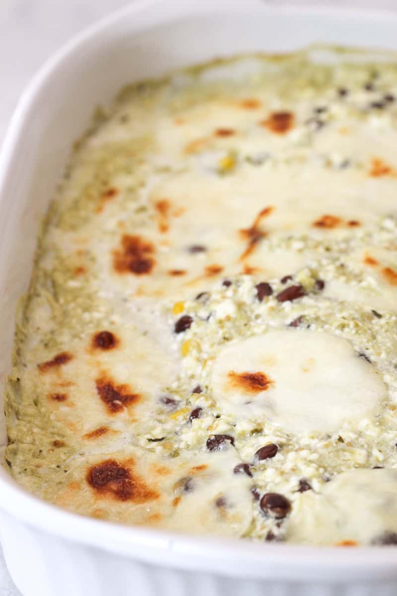 A close-up of a baked casserole dish with a creamy, greenish mixture and browned cheese spots on the surface.