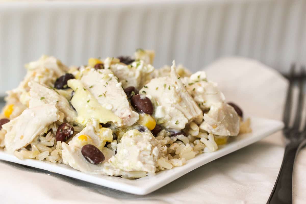 A plate of rice topped with chunks of chicken, black beans, corn, and creamy sauce, garnished with herbs.