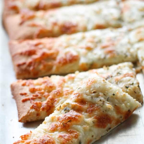 Sliced rectangular pieces of cheesy bread topped with herbs on a metal tray.