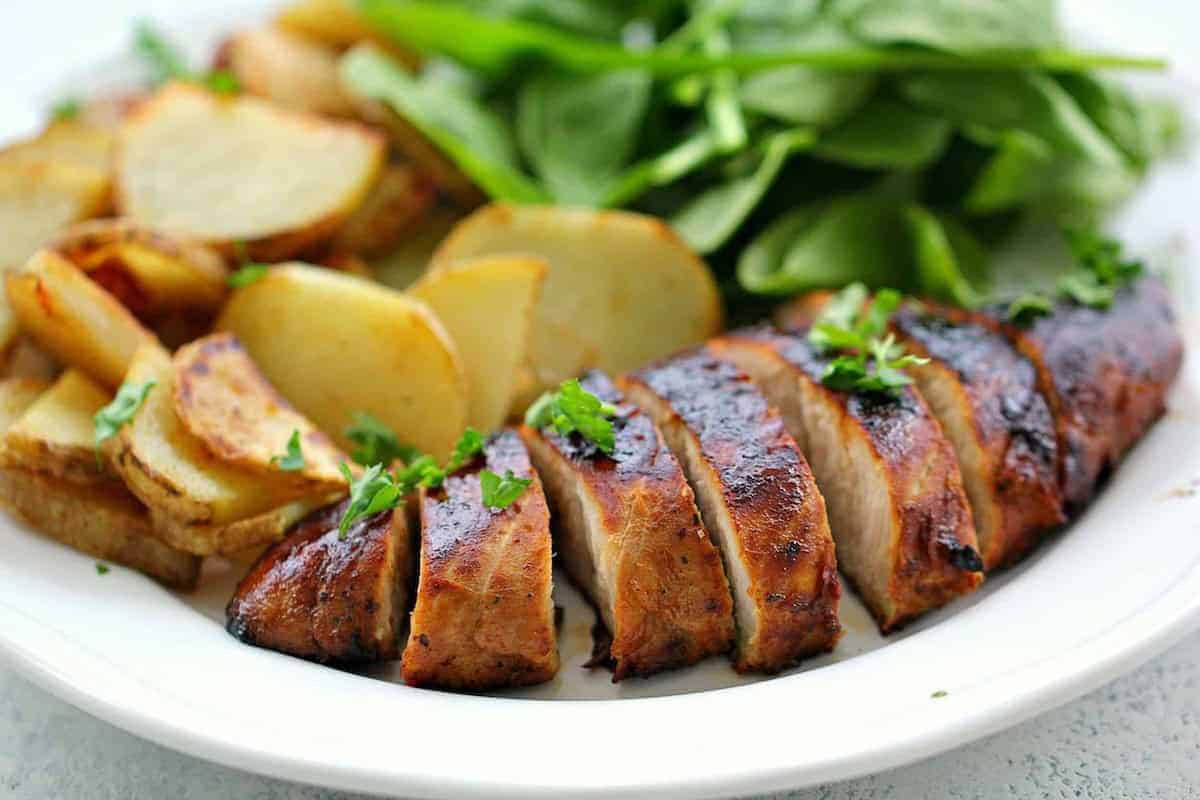 A plate with sliced marinated turkey breast, seasoned potato wedges, and fresh green spinach leaves.