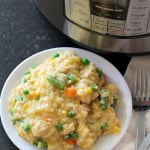 A white plate with a serving of creamy rice dish mixed with peas, carrots, and corn with Instant Pot appliance in the background.