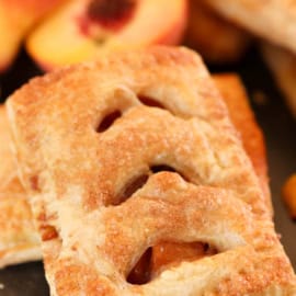 Baked Peach Hand Pie laying on top of another hand pie with cut fresh peaches in the background.