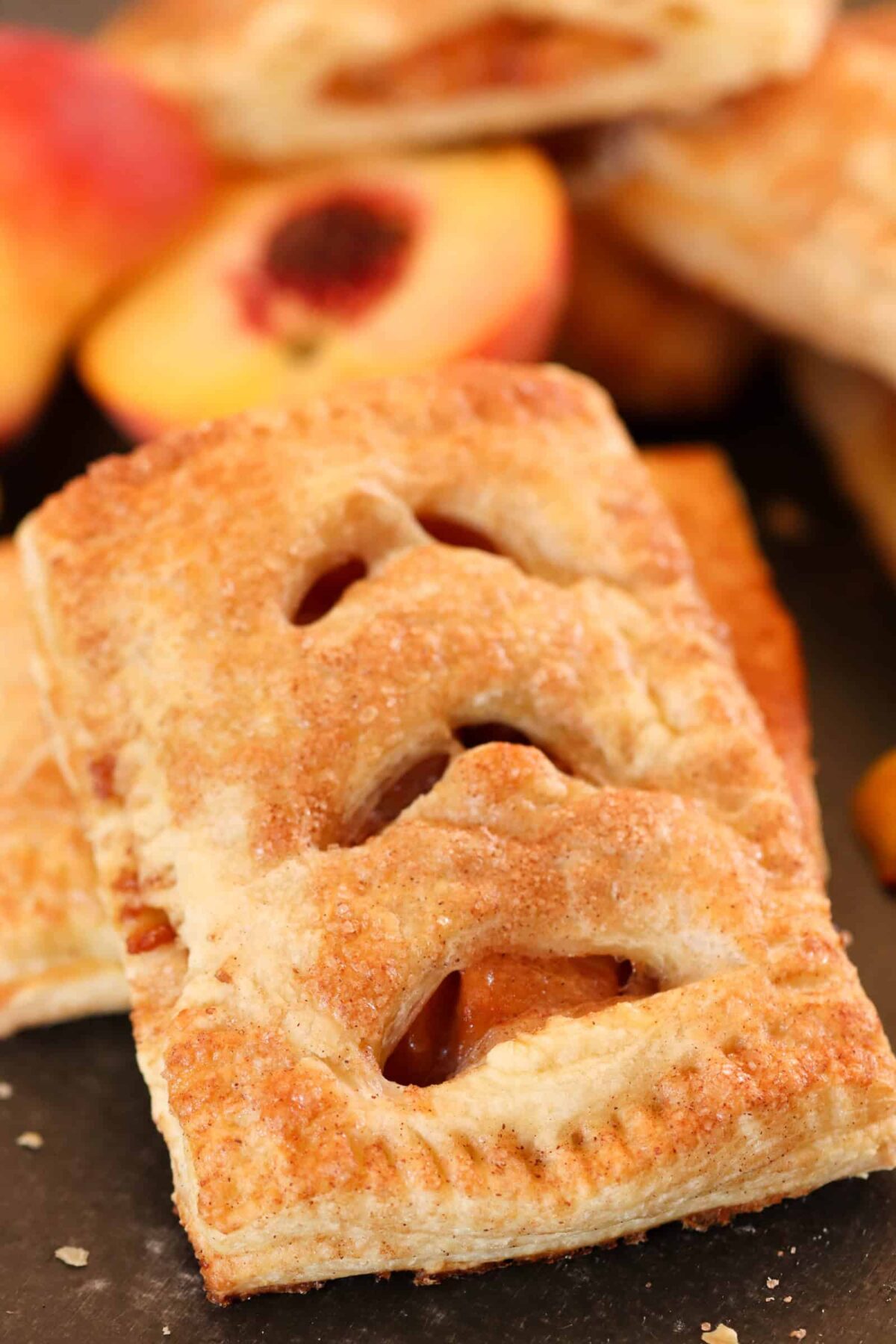 Baked Peach Hand Pie laying on top of another hand pie with cut fresh peaches in the background.