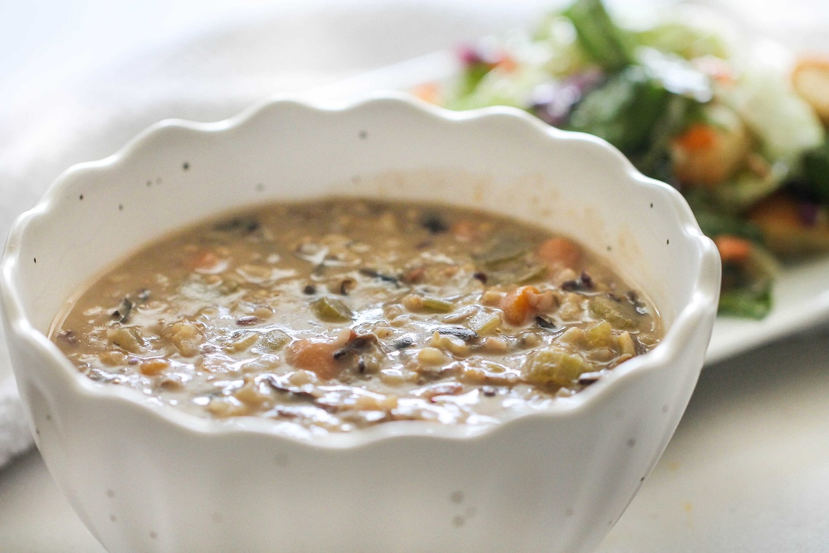 A bowl of creamy vegetable and wild rice soup is placed in front of a plate with a green salad.