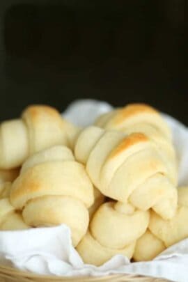 A basket filled with freshly baked dinner rolls on a white cloth.