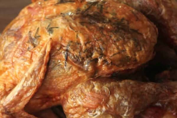 A whole roasted chicken with crispy skin, garnished with herbs, placed on a white plate.