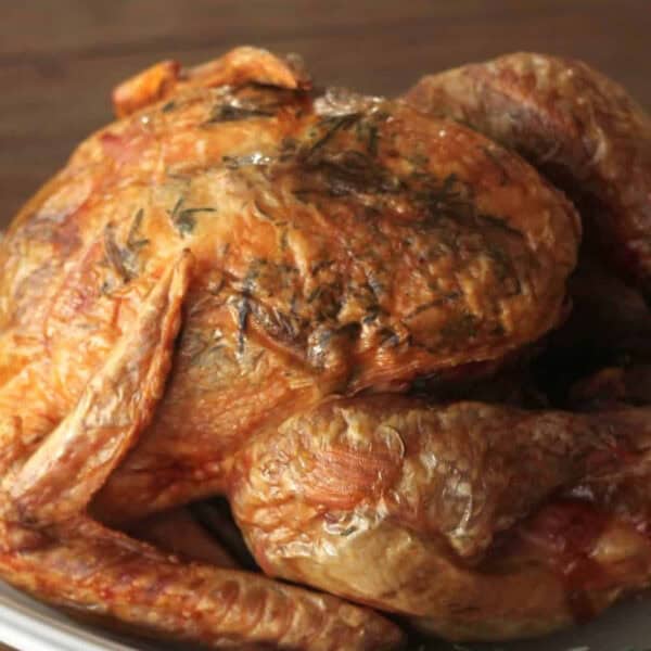 A whole roasted chicken with crispy skin, garnished with herbs, placed on a white plate.