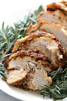 Sliced Instant Pot Turkey Breast garnished with fresh rosemary on a white plate.