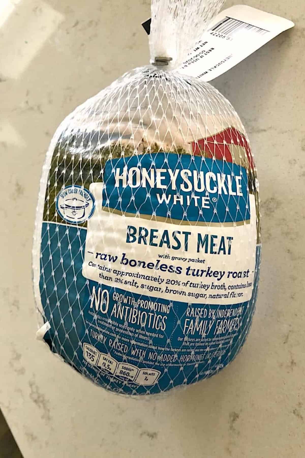 A packaged Honeysuckle White turkey breast meat labeled as raw boneless turkey roast, wrapped in a net bag, placed on a light-colored surface.