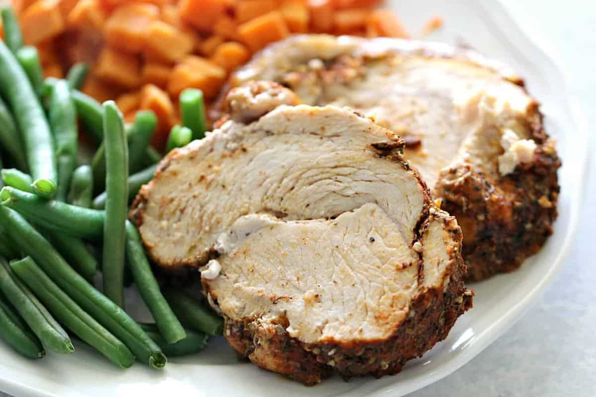 Close-up of a plate featuring two slices of roasted turkey breast, green beans, and diced sweet potatoes.