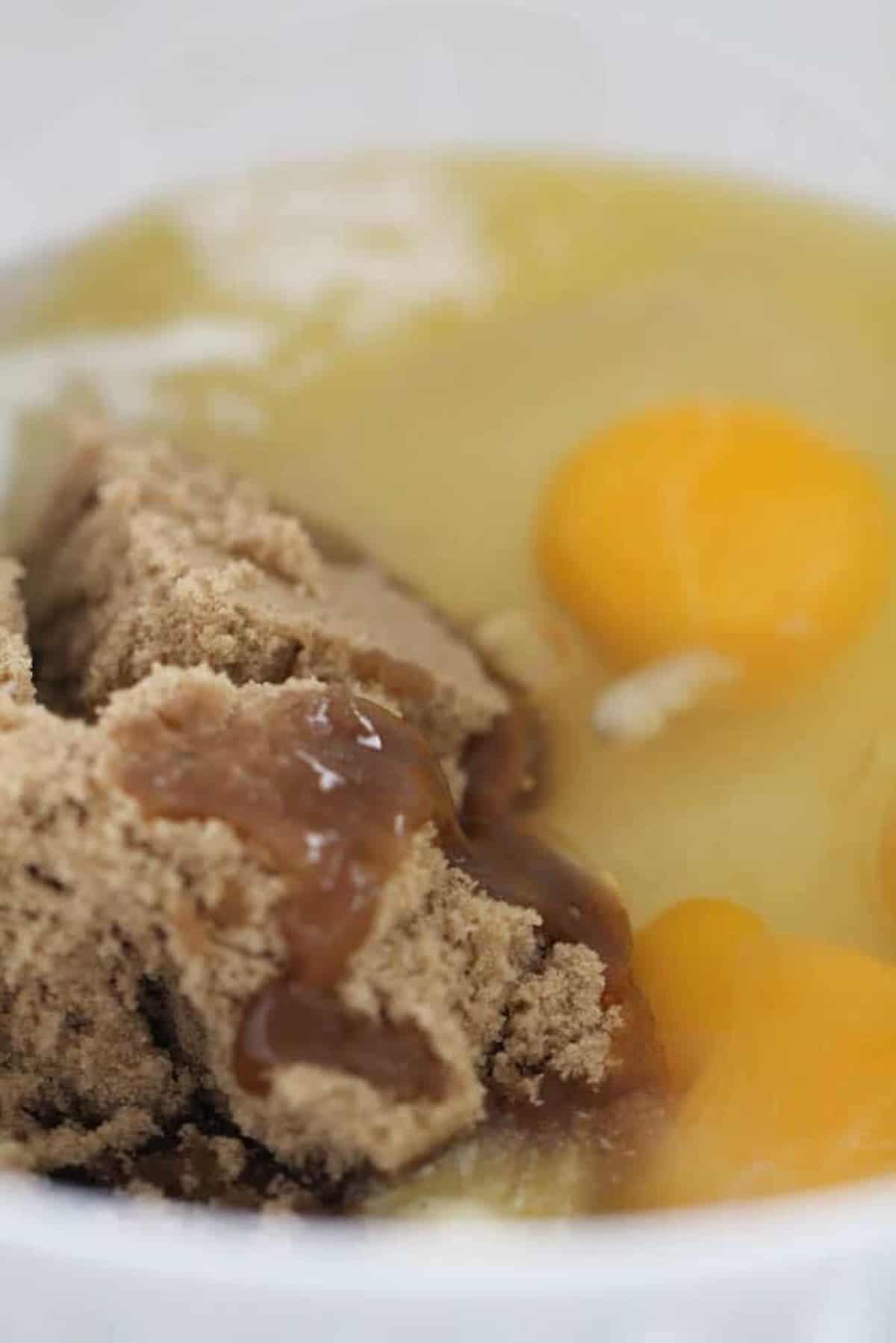 A bowl containing brown sugar, two egg yolks, and melted butter.