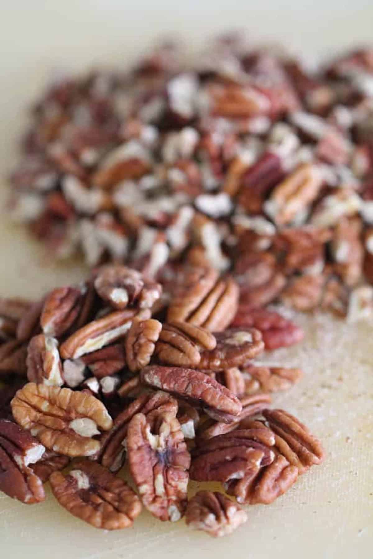 Close-up image of a pile of chopped pecans on a light-colored surface.