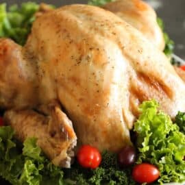 A roasted turkey garnished with leafy greens and cherry tomatoes on a dark surface.