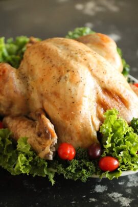 A roasted turkey garnished with leafy greens and cherry tomatoes on a dark surface.