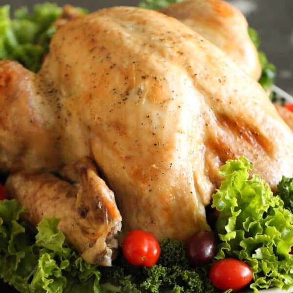 A roasted turkey garnished with leafy greens and cherry tomatoes on a dark surface.