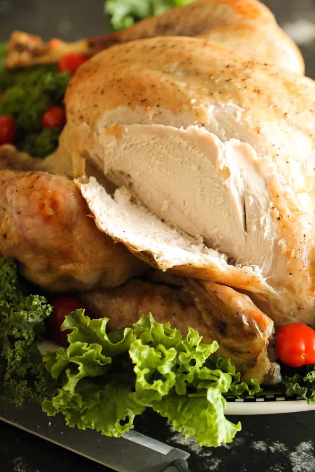 Roasted turkey with a slice cut, surrounded by leafy greens and cherry tomatoes.