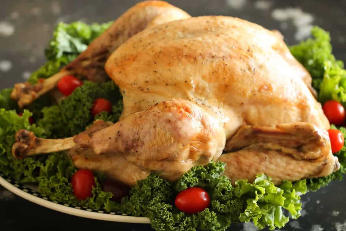 A cooked turkey on a platter garnished with kale leaves and cherry tomatoes.