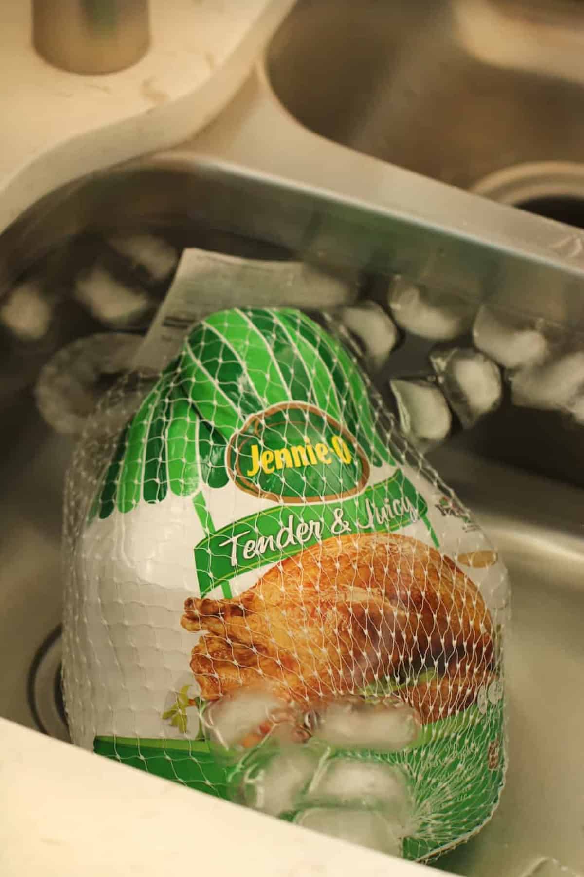 Frozen turkey in packaging sits in a sink surrounded by ice cubes.