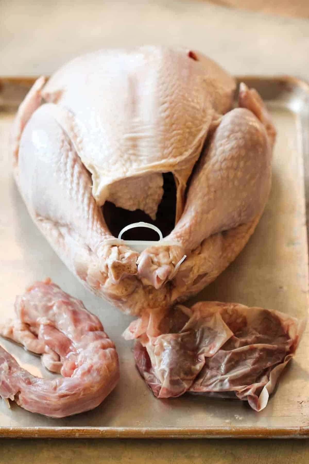 Raw whole turkey with giblets and neck placed beside it on a metal tray.