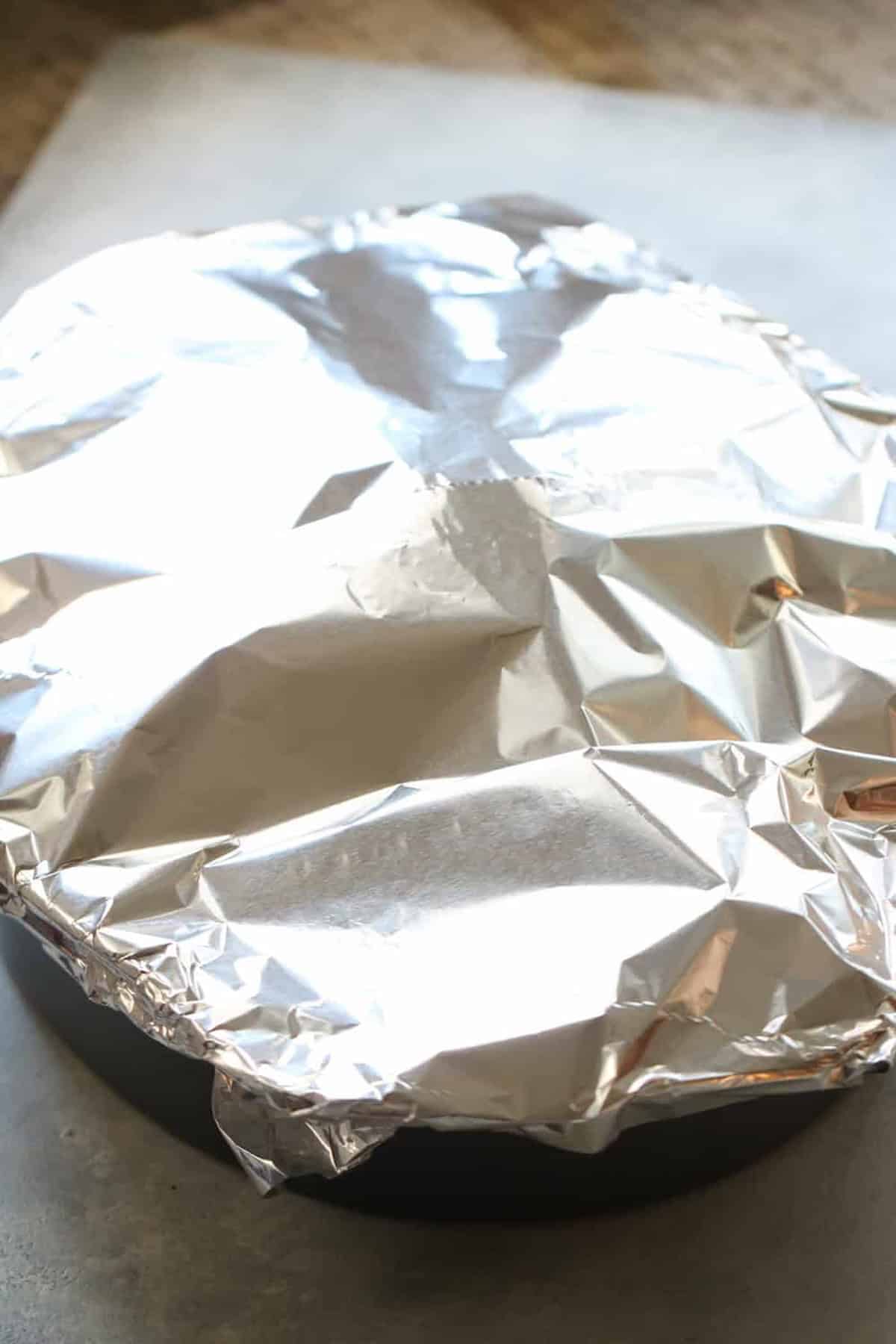 A foil covered turkey in a roasting pan